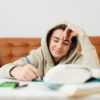 Подросток в капюшоне делает уроки за столом с книгами
